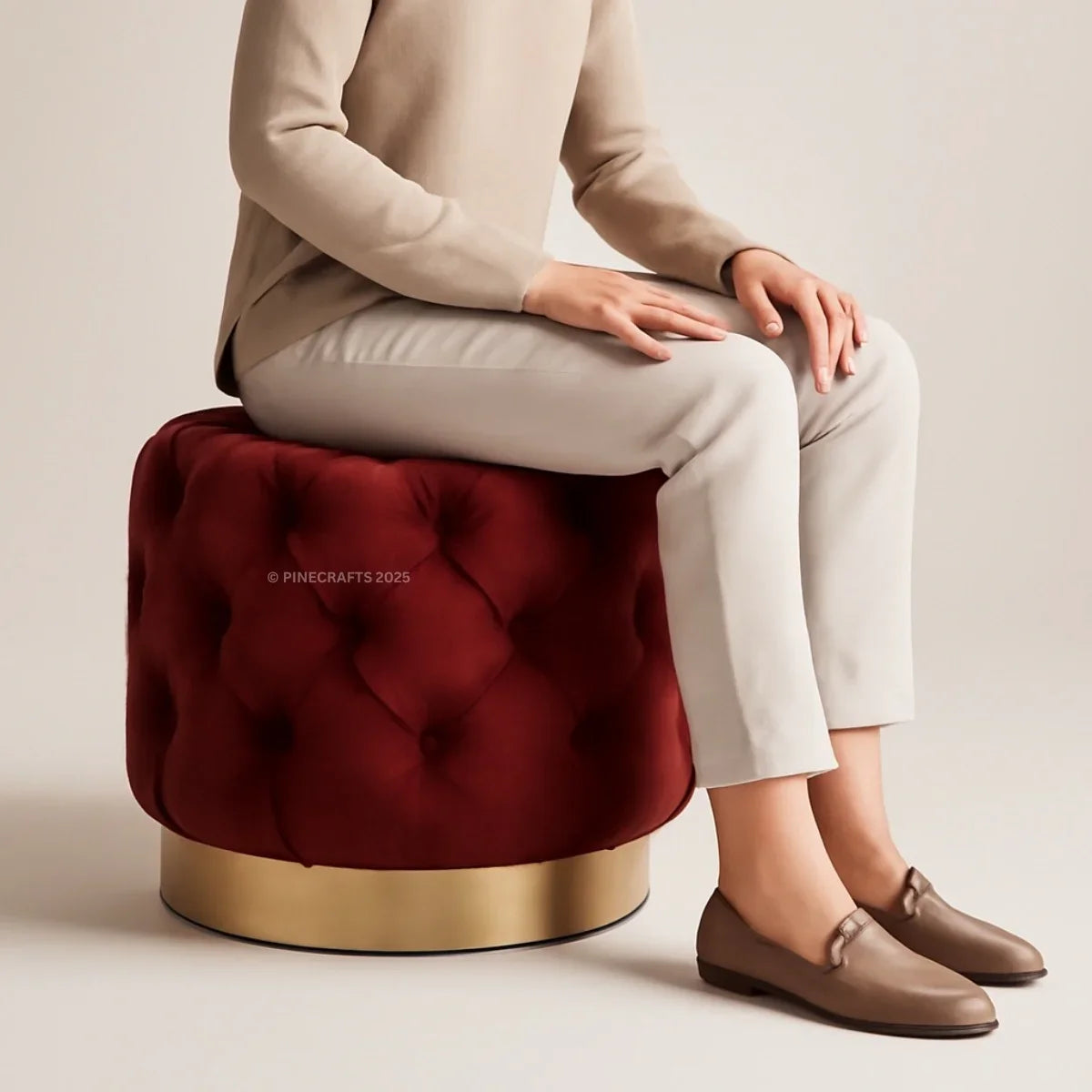 Person sitting on a red tufted stool with a gold base against a beige background